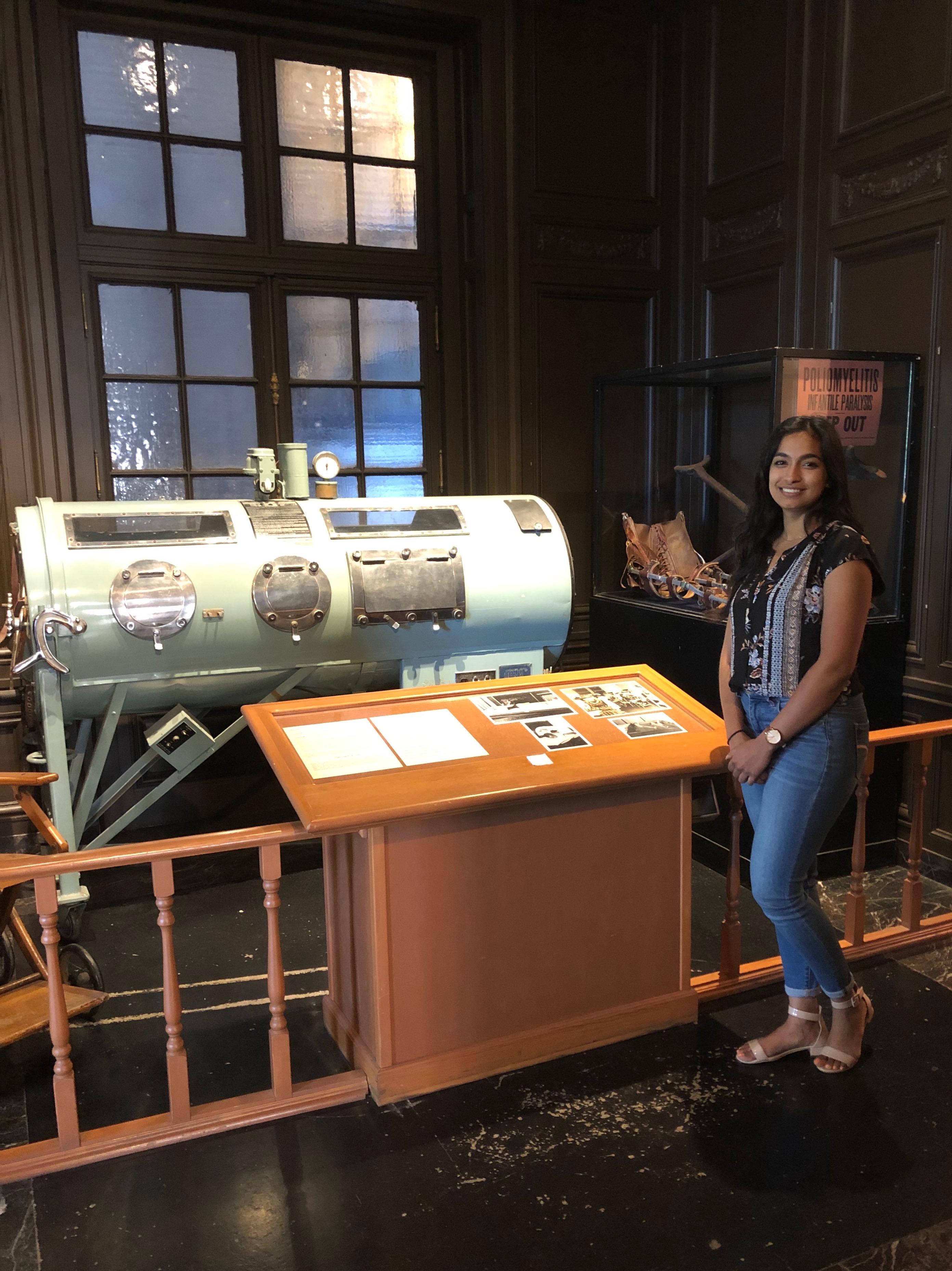 Anu standing next to the light blue iron lung displayed in the polio exhibit